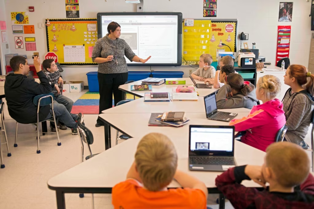 Teacher guiding students working on laptops in a classroom