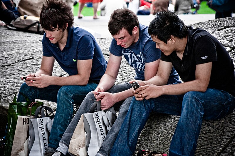 Three young men absorbed in their mobile phones on a busy street