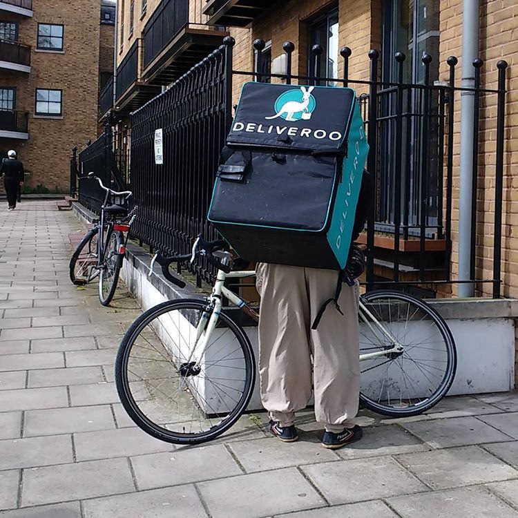A Deliveroo food delivery cyclist riding through London, wearing a branded backpack